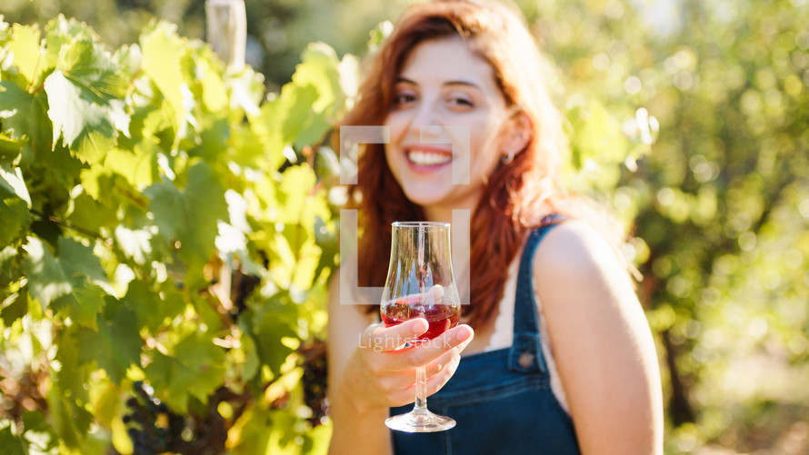 Beautiful red hair girl smile with glass of wine among vineyards in countryside