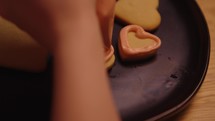 Young woman decorates heart shaped cookies with icing and sprinkles for valentines day