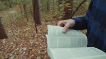 a man carrying a Bible walking into the woods in fall 