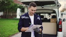 Delivery service worker makes notes on documents and standing on the street near the minivan.