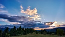 Epic sunset with colorful clouds, Golden hour at sunset. Epic hilly clouds. Mountain forest landscape with meadows full of flowers