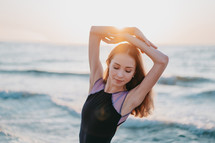 Portrait of young woman with long hair practicing classic exercises with emotions.Dancing ballerina in black silk dress on embankment near ocean or sea at sunrise or sunset
