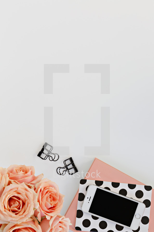 journals, peach roses, phone, and clips on a white desk 