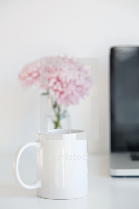 coffee cup, vase of flowers, and laptop computer on a desk 