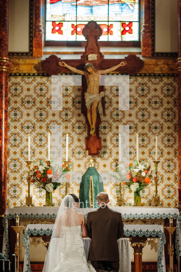 crucifix above a kneeling bride and groom 