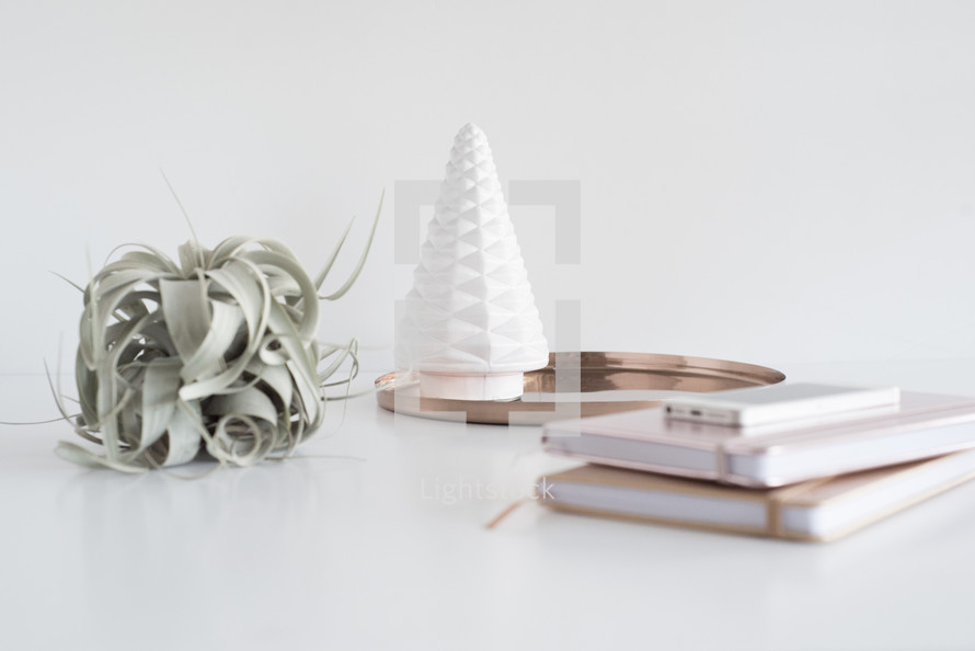 white tree figure, gold tray, plant, journals, and cellphone on a desk 