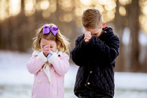 girl and boy child praying outdoors in snow 