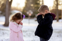 girl and boy child praying outdoors in snow 