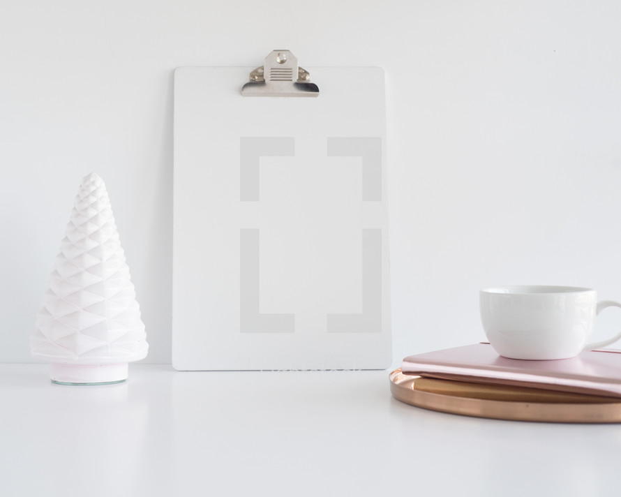 white figure, clipboard, gold tray, journals, and coffee cup 