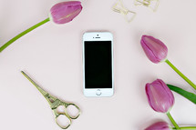 iPhone, scissors, gold paperclips, and fuchsia tulips on a pink background 