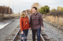 portrait of a couple standing in the middle of train tracks 