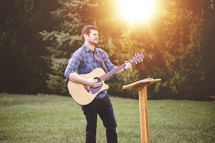 a man playing a guitar outdoors in front of a podium 