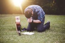 a man with a guitar praying outdoors reading a Bible 