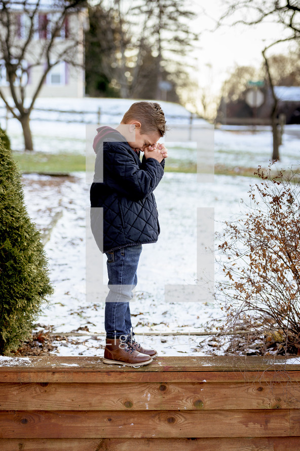 boy child praying outdoors in snow 