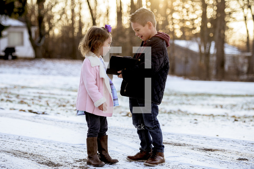 girl and boy child holding a Bible outdoors in snow 