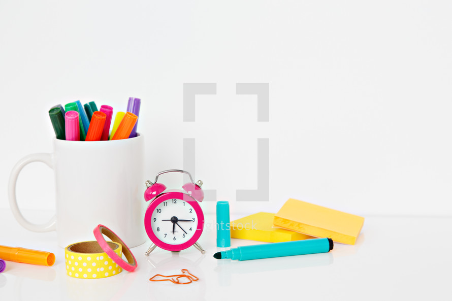 alarm clock, mug of markers, and paperclips on a white background 