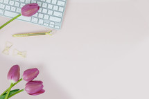 computer keyboard, pen, gold paperclips, and fuchsia tulips on a pink background 