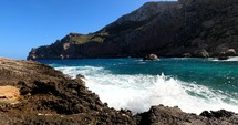 Pan hyper lapse of waves hitting the coast of Mallorca, mountains in background, sunny day, in Balearic islands, Spain