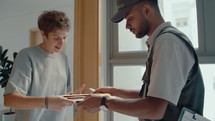 Young woman signing delivery document, receiving express mail and saying goodbye to male courier. Medium shot
