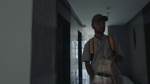 Delivery man with backpack going through corridor in residential building, carrying bag with food and drinks, ringing the doorbell
