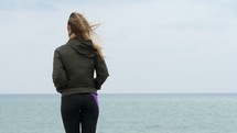 Woman looking out into the ocean in exercise clothes with wind blowing her hair.