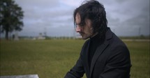 Young man kneeling in black suit looking at cross praying in worship in cinematic slow motion.