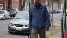 a elderly man wearing a face mask walking on a sidewalk 