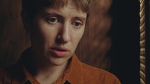 Young woman telling about her sins to priest through perforated screen of confession booth during private talk in church
