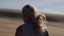a woman walking up sand dunes in a desert 