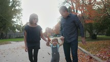 grandmother, grandfather, and granddaughter walking holding hands in fall 