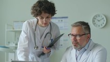 Senior Doctor Discussing Data on Laptop with Young Female Assistant
