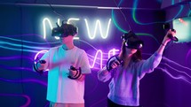 A man and a woman move their arms around as they play a virtual reality game with goggles.