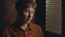 Young female penitent sitting in confessional stall and talking to priest through perforated screen when confession her sins
