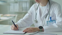 Female Doctor Writing Medical Report at Desk in Clinic
