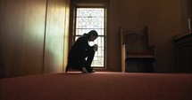 Man kneeling to pray in front of stained glass window. Young man praying, confessing sin, worshipping in church in cinematic slow motion.