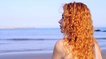 a woman with red hair standing on a shore 