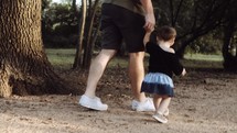 father and toddler daughter walking on a path 