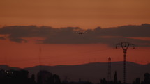 The airplane flying over the power transmission lines, electric poles, and wires, with the sky after sunset
