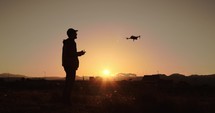 Silhouette of man pilot a drone with remote controller in the nature at sunset