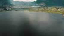 Tilt-up shot of Misty Atmosphere In The Placid San Pablo Lake, Imbabura Stratovolcano And San Pablo Del Lago Village In Ecuador.
