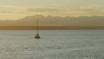 Birds fly by sailboat on water in front of mountain range during sunset, slow-motion