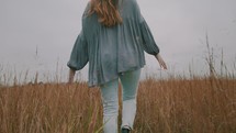 a woman walking through a field of tall grasses 