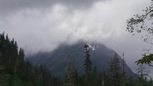 Clouds move across mountain peak on cloudy day with forest below