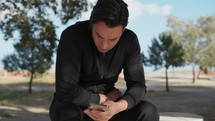 Seated Man In The Park Using Smartphone Under The Trees