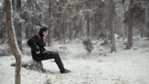 a man sitting on a rock in a forest in the falling snow 