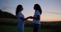 Two girls praying at dusk in a field 1