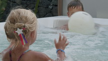 Brother with little sister playing ball in hot tub