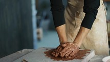 A male potter kneads brown clay on a special board. Professional everyday life.