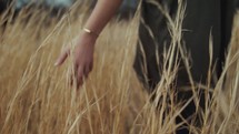 a young woman walking through a field of tall brown grasses 