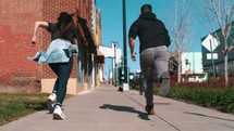 a girl and guy racing down a sidewalk in a city